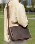 Back view of a dark brown leather satchel bag worn by a model, highlighting padded strap and minimalistic design