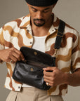 Close-up of a black crossbody bag with its flap open, showing the snap closure and zippered compartment.