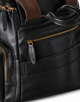 Black full-grain leather backpack top closure with a gold-tone double zipper and leather pulls