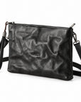 Black leather clutch bag with a crinkled texture, featuring a top zipper closure, a detachable wristlet strap, and a matching adjustable shoulder strap with silver hardware.