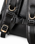 Close-up of a black pebbled leather bag with black webbing straps, gold-tone metal D-rings, and black plastic buckle.