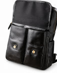 Black faux-leather backpack with two front flap pockets secured by gold-tone snap buttons.