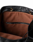 Close-up of the interior of a black leather bag, showing a brown fabric lining with a front slip pocket and gold-tone grommets.