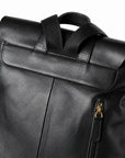 Close-up of a black faux-leather backpack showing the top flap, dual top handles, and a gold-tone zipper.