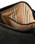 Close-up of the interior of a black leather bag, showing a tan and beige striped fabric lining with a zippered pocket.