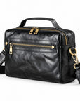 Black leather crossbody bag with gold-tone hardware, featuring a top handle, a front zippered pocket, and an adjustable shoulder strap.