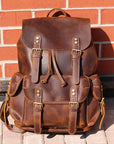 Brown leather backpack against a brick wall