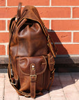 Brown leather backpack against a brick wall