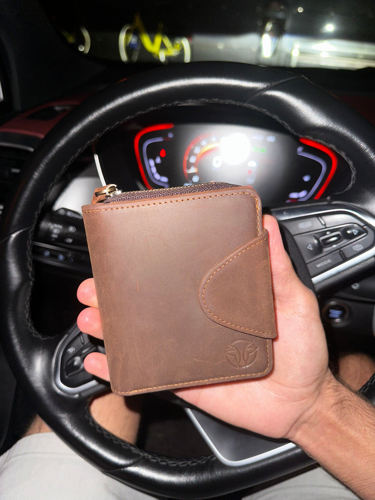 Brown leather wallet held in hand inside a car, showcasing its stylish design and practicality.