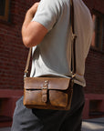 Person wearing a brown leather bag against a brick wall.