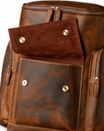 A brown distressed leather backpack with a front flap pocket featuring brass snap buttons and a main zippered compartment.