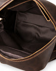 Close-up of an open dark brown leather bag showing the interior lining, gold-toned zipper, and stitching details.