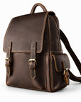 A dark brown leather backpack with brass-tone hardware, featuring a top handle, front flap with buckle straps, a zippered main compartment, and a side pocket.