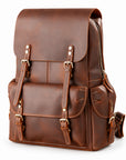 A brown leather backpack with a front flap, buckle straps, and multiple pockets, photographed.