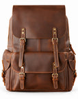 A brown leather backpack with front buckle straps and multiple pockets, photographed against.