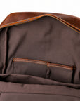 Close-up of the interior of a brown leather and fabric backpack, showing a zippered opening, interior pockets, and contrast stitching.