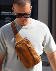 brown leather sling crossbody bag worn by man in street style outfit, compact everyday carry bag