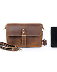 Brown leather bag with strap and smartphone on a white background