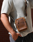 Person wearing a brown leather crossbody bag against a brick wall