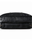 The underside of a black leather briefcase shows its two-section construction, central seam and piped edges.
