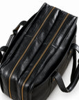 A top view of the black leather briefcase shows two parallel brass-tone zippers and folded carry handles.