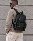 Classic black leather backpack for men with multiple exterior pockets, buckle closures, top handle and adjustable shoulder straps