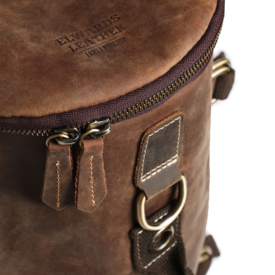 Close-up of the top section of a handcrafted leather backpack, showing stitching, sturdy zippers, and durability for travel.