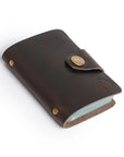 Dark brown leather card holder with button clasp and minimalist design, handcrafted for elegance and durability.