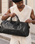 Durable black leather duffle bag for men with top handles, side zip pocket, luggage tag and spacious travel compartment