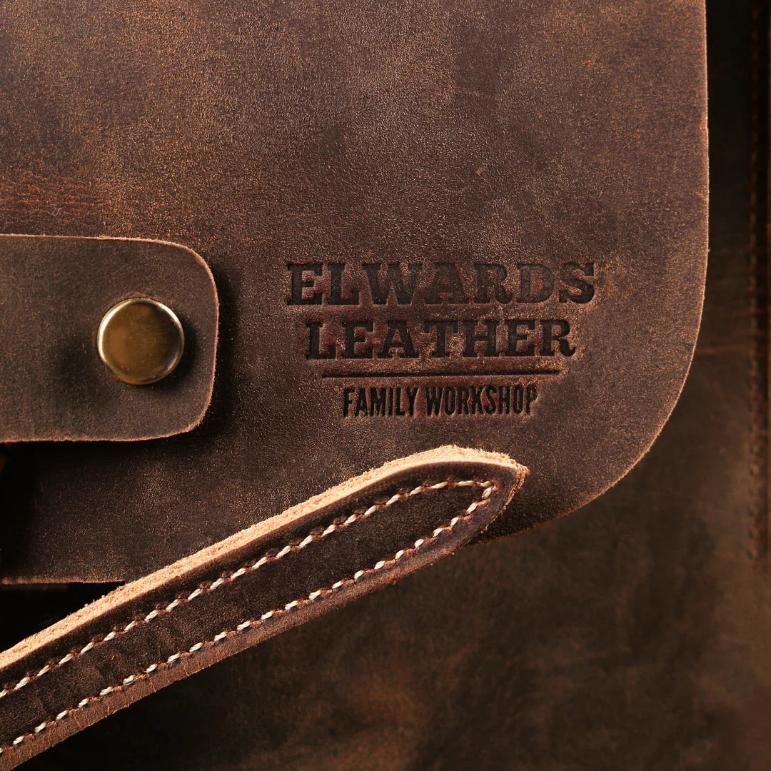 Close-up of the Elwards Leather logo on a vintage brown backpack, highlighting the brand and leather texture.