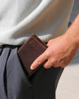 Person holding a brown leather wallet in their pocket with a blurred background