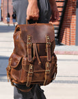 Brown leather backpack held by a person outdoors.
