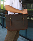 Man carrying a brown handmade leather messenger bag with a shoulder strap, showcasing its vintage design.