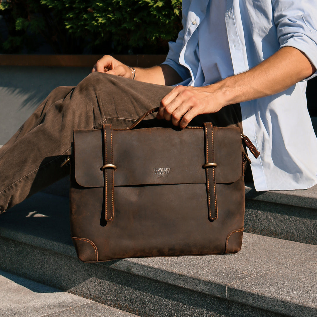 A man sitting with a vintage leather messenger bag, demonstrating its timeless design and practicality.
