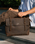 A man sitting with a vintage leather messenger bag, demonstrating its timeless design and practicality.
