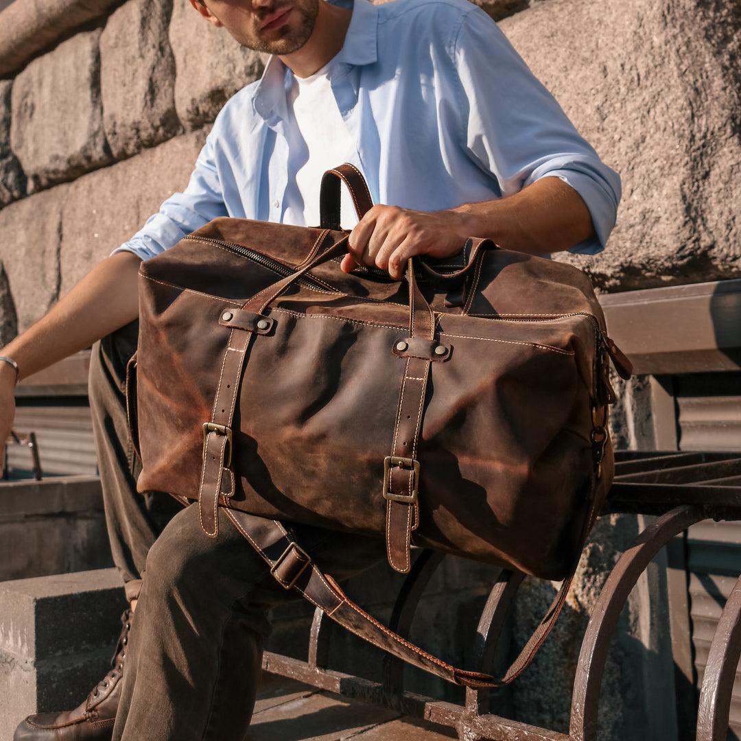 Man sitting outdoors with vintage handmade weekender bag, emphasizing its durable crazy horse leather and timeless style.