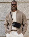 Man wearing a black leather crossbody bag with gold-tone hardware and adjustable strap