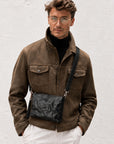 Man wearing a textured black leather crossbody bag with adjustable shoulder strap