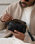 Close-up of a black leather crossbody bag with gold zipper and interior zip pocket