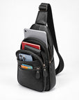 Black pebbled leather crossbody bag with a single shoulder strap, shown open with a tablet, phone, wallet, and cards inside, on a clean white studio background.
