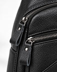 Close-up of a black pebbled leather bag showing a silver zipper with a leather pull tab and metal hardware on a light gray background.