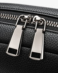 Close-up of a black pebbled leather bag with two silver metal zipper pulls and a silver zipper track.