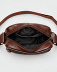 A brown textured leather crossbody bag shown open from a top-down view, displaying its black interior lining and adjustable strap on a light gray background.