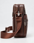A brown textured leather crossbody bag with multiple zippered compartments and an adjustable woven strap, shown from a side profile view on a light gray background.