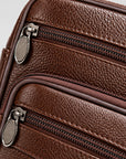 Close-up of a brown pebbled leather bag showing two silver-tone zippers with oval pull tabs and fine stitching.