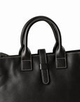 Men's black full-grain leather tote bag handle detail with contrast stitching and a central leather tab
