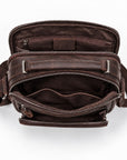 An overhead view of a dark brown leather crossbody bag shown open to display its interior compartments, pockets, and zipper details against a clean white background.