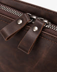 Close-up of a dark brown leather zippered pouch with two leather pull tabs and silver metal hardware.
