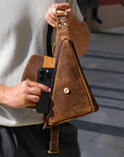 Person holding a brown leather bag with a phone case on a blurred background