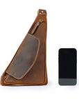 Brown leather sling bag next to a smartphone on a white background